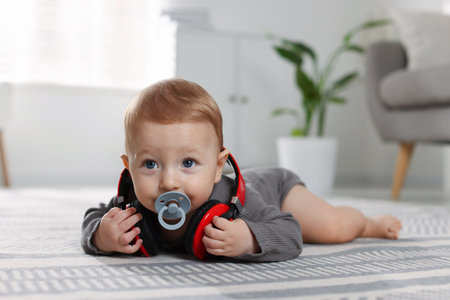 Cute little baby with pacifier and headphones on floor at homeの写真素材