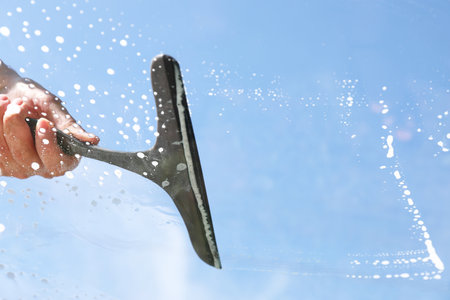 Woman washing window with squeegee tool against blue sky, closeup