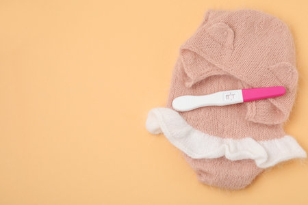 Pregnancy test and baby clothes on pale orange background, top view. Space for textの写真素材