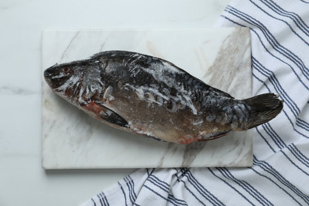 Frozen carp fish on white marble table, top view