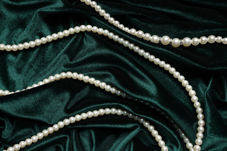 Beautiful pearl necklace on green cloth, top view