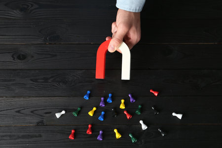 Man with magnet attracting different colorful game pieces at black wooden table, above viewの写真素材
