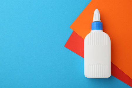 Bottle of glue and colorful paper on light blue background, top view. Space for textの写真素材