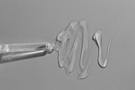 Dripping cosmetic serum from pipette on gray background, top view