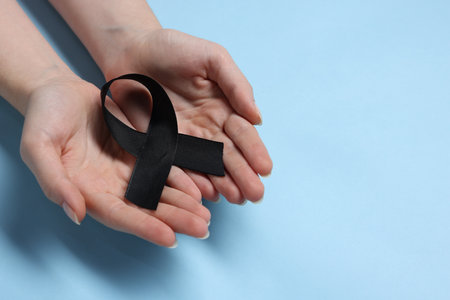 Woman with black ribbon on light blue background, closeup with space for text. Melanoma and mourning conceptの写真素材