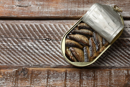 Tasty sprats in tin can on wooden table, top view. Space for text