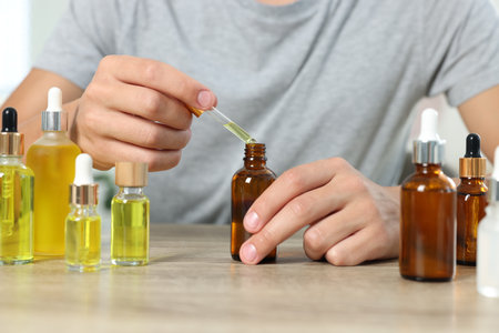 Young man dripping CBD tincture into bottle from dropper at wooden table, closeupの写真素材