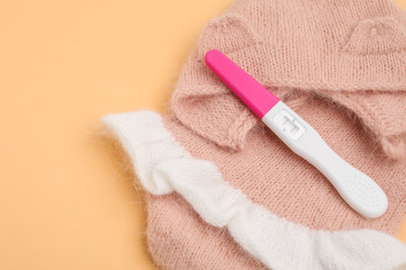 Pregnancy test and baby clothes on pale orange background, closeupの写真素材