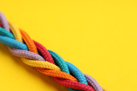 Braided colorful ropes on yellow background, closeup with space for text. Unity concept