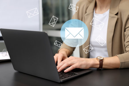 Woman using laptop at table, closeup. Envelopes as symbol of message over computerの写真素材