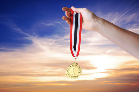 Woman holding gold medal in hand against sunset sky, closeupの写真素材