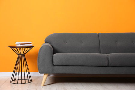 Stylish sofa and side table with books near orange wall indoorsの写真素材