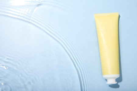 Cosmetic product. Tube with cream in water on light blue background, top view. Space for textの写真素材