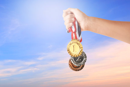 Woman holding gold, silver and bronze medals in hand against sky, closeupの写真素材