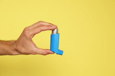 Man holding asthma inhaler on yellow background, closeup. Space for textの写真素材