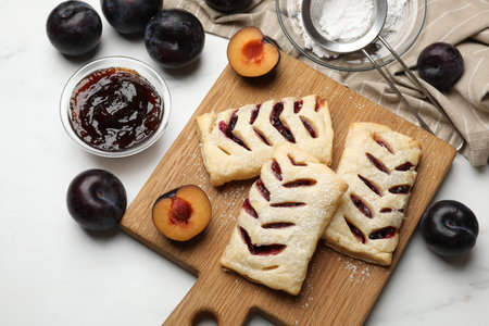 Delicious puff pastries and plums on white wooden table, flat layの写真素材