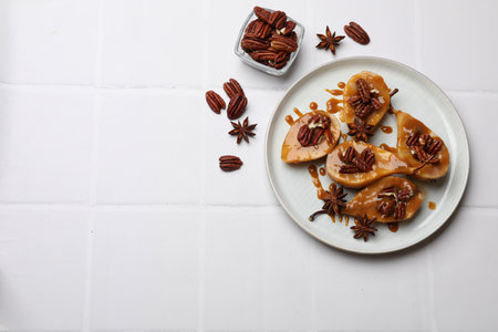 Delicious pears with caramel sauce, pecan nuts and anise stars on white tiled table, top view. Space for textの写真素材