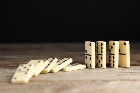 Domino effect. Tiles falling on wooden table against black background, closeupの写真素材