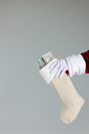 Santa Claus holding stocking with dollar banknotes on gray background, closeup