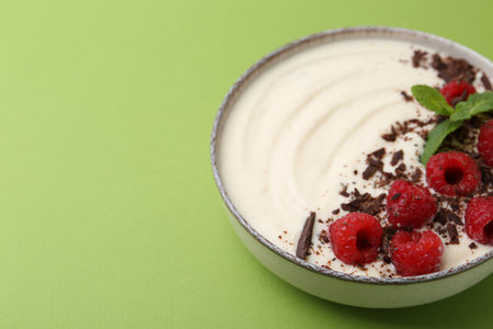 Tasty cooked semolina porridge with raspberries, chocolate and mint on green background, closeup. Space for textの写真素材