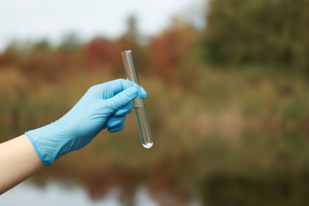 Examination of water quality. Researcher holding test tube with sample outdoors, closeup. Space for textの写真素材