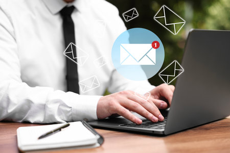 Man using laptop at table, closeup. Envelopes as symbol of message over computerの写真素材