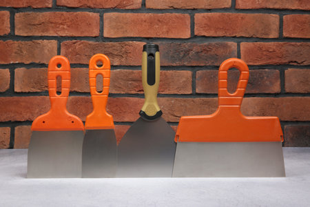 Different trowels on light textured table against red brick wall. Construction tools