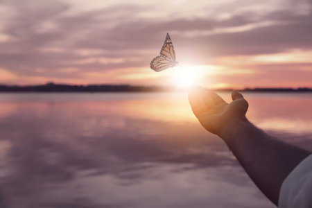 Man and butterfly near river at sunset, closeup. Health, spring, freedomの写真素材