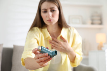 Young woman with asthma inhaler at home, selective focusの写真素材