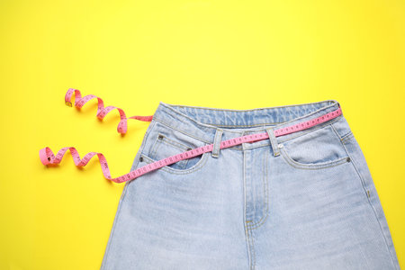 Jeans and measuring tape on yellow background, top viewの写真素材