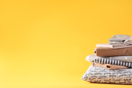 Stack of clean bed linen and pillow on yellow background. Space for textの写真素材