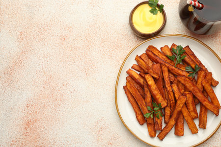Delicious sweet potato fries, parsley, sauce and soda drink on beige textured table, top view. Space...