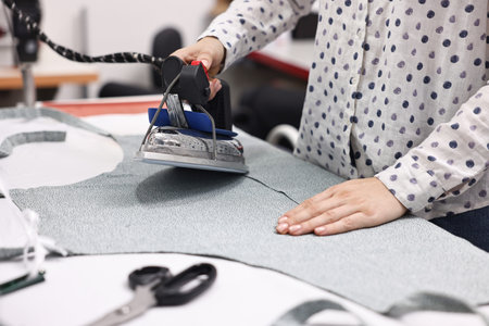 Young woman with iron working at white table in professional workshop, closeupの写真素材