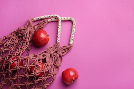 Handmade macrame shopping bag with apples on crimson background, top view. Space for textの写真素材