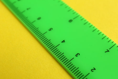 One green ruler on yellow background, closeup