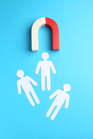 Magnet attracting paper cutouts of humans on light blue background, flat layの写真素材