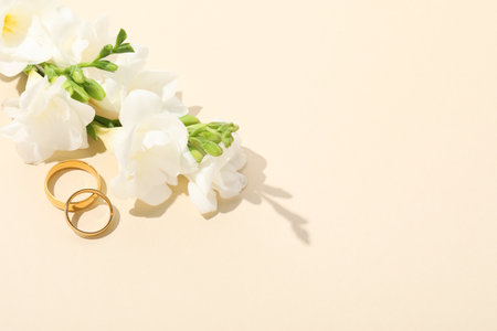 Golden wedding rings and flowers on beige background, space for textの写真素材