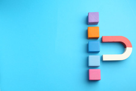 Magnet attracting colorful cubes on light blue background, flat lay. Space for textの写真素材