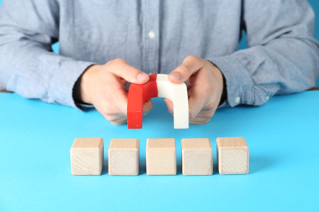 Man with magnet attracting wooden cubes on light blue background, closeupの写真素材