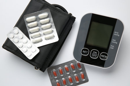 Blood pressure measuring device and pills on white background, top view