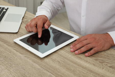 Businessman using tablet at wooden table, closeup. Modern technology
