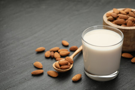 Fresh almond milk in glass, spoon and nuts on black table, closeupの写真素材