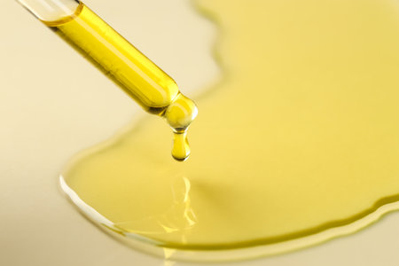 Cosmetic oil dripping from pipette on dark beige background, closeup. Space for textの写真素材