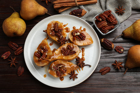 Delicious pears with caramel sauce, pecan nuts and spices on wooden table, flat layの写真素材