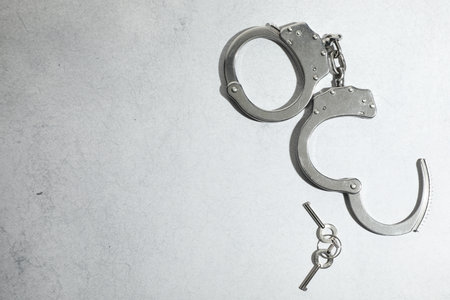 Metal chain handcuffs and keys on light gray table, top view. Space for text