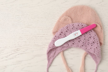 Pregnancy test and baby hats on white wooden table, flat lay. Space for textの写真素材