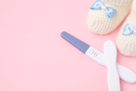 Pregnancy tests and knitted booties on pink background, closeup. Space for textの写真素材