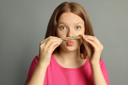 Funny teenage girl with tasty rainbow sour belt on gray backgroundの写真素材