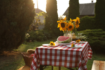 Vase of sunflowers, watermelon and plates on table in gardenの写真素材