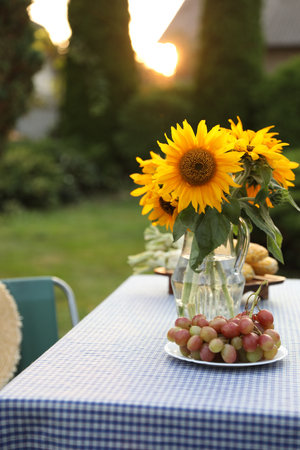 Vase of sunflowers, corn and grapes on table in gardenの写真素材